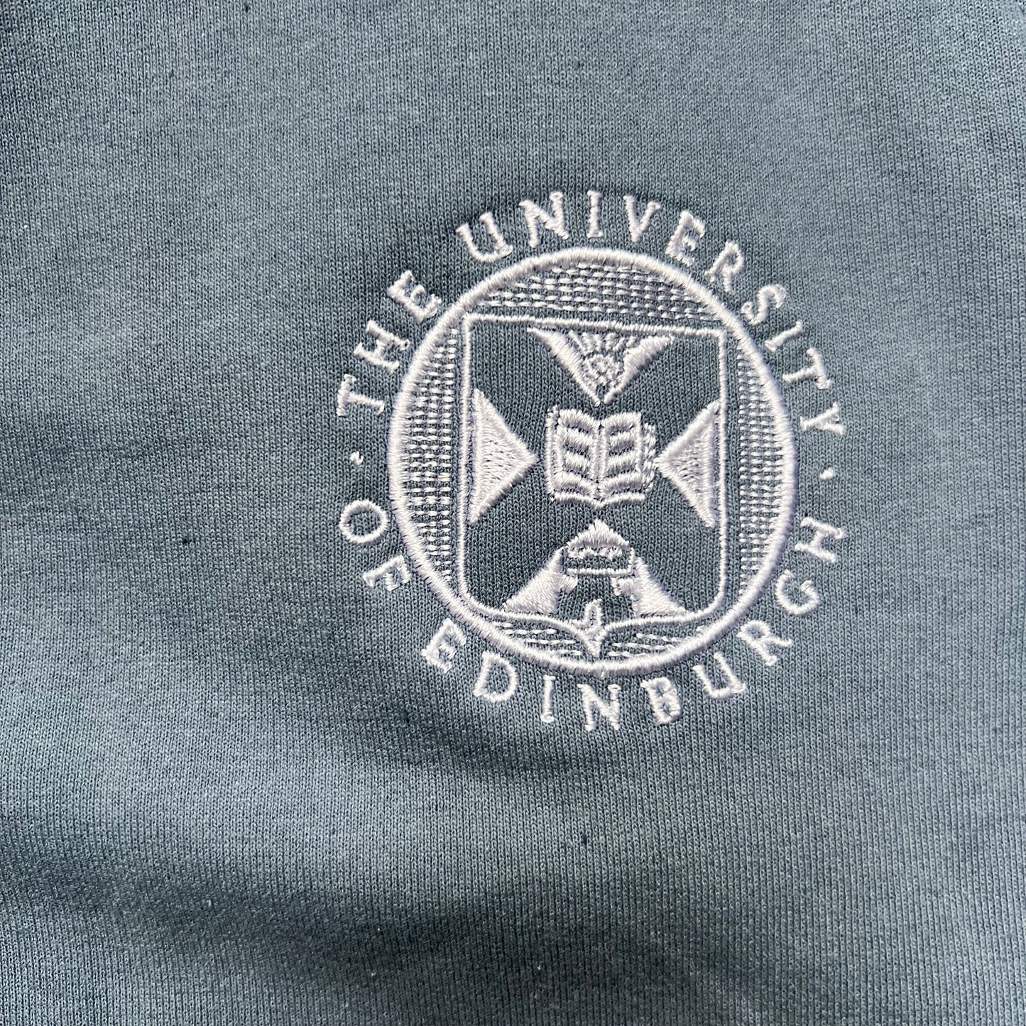 Close up of university crest embroidered in white on stone blue jogging bottoms