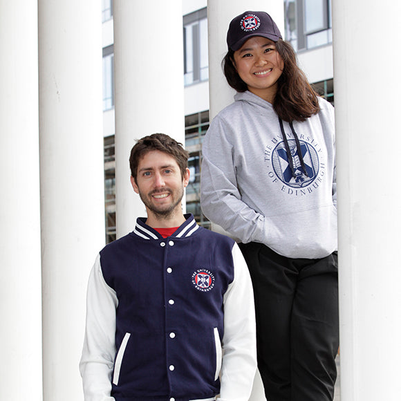 Two models wearing University merchandise. The model on the left is wearing a Varsity Style Baseball Jacket while the right hand model is wearing a Large Crest Two Tone Hoodie in navy and our Embroidered Crest Cap.  