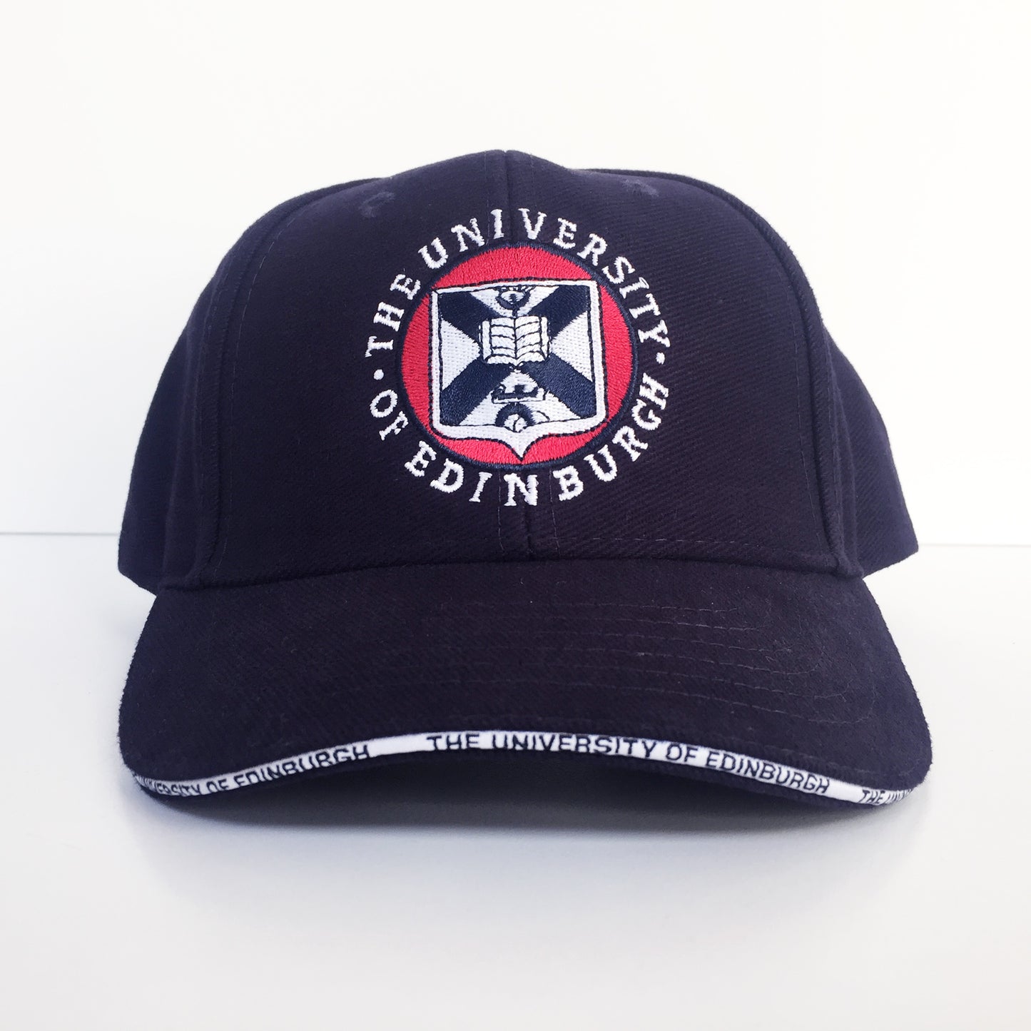 Alternate angle of the navy embroidered cap which demonstrates the white piping on the visor that reads 'The University of Edinburgh' 