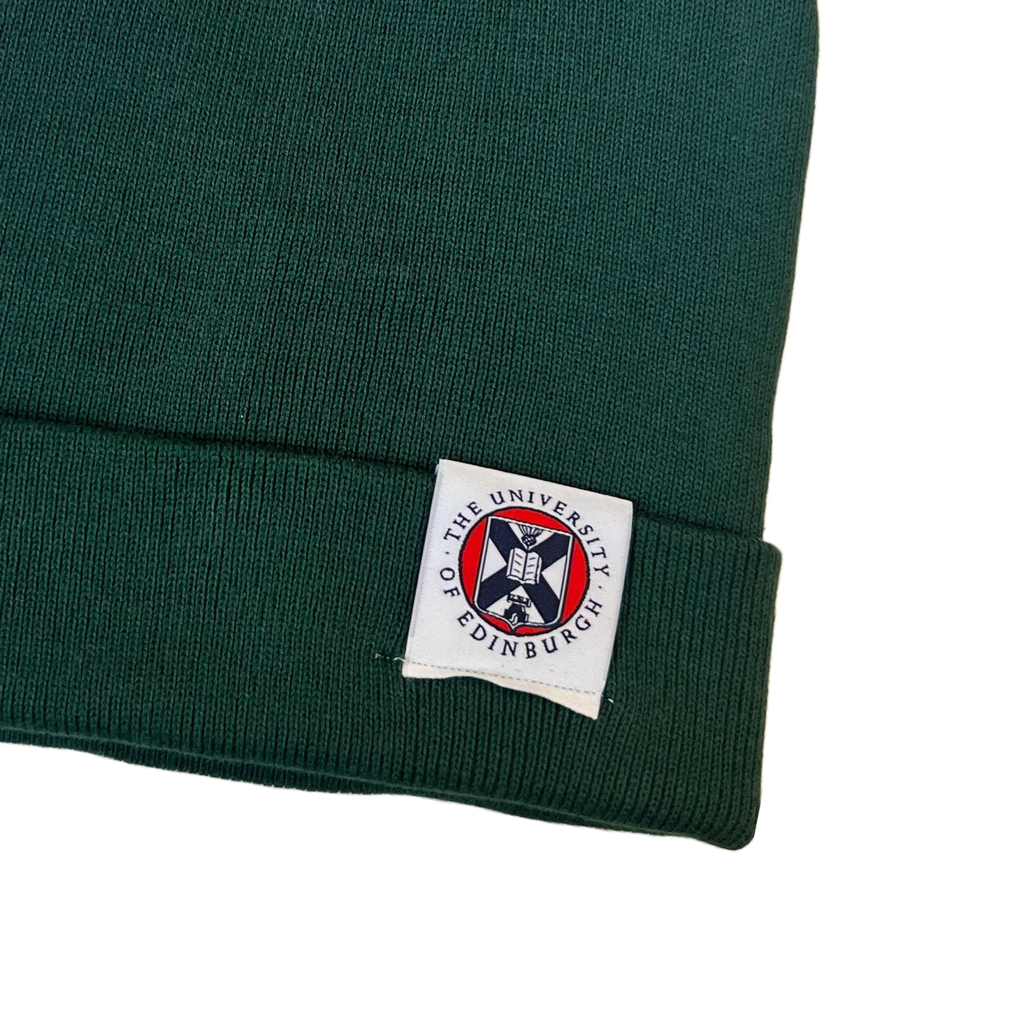 close up of bottle green rubbed beanie with woven label featuring University crest in red white and navy