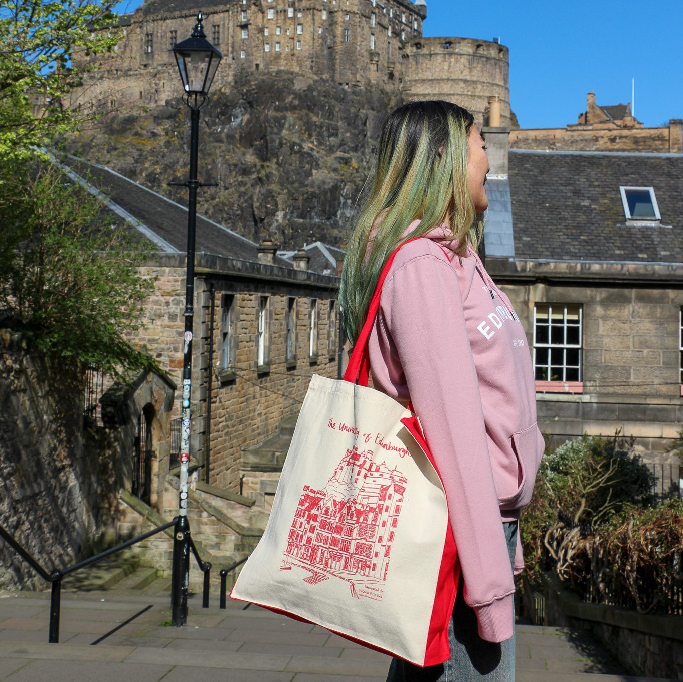 Our model holding the castle design premium tote bag and wearing the established print hoodie in purple rose