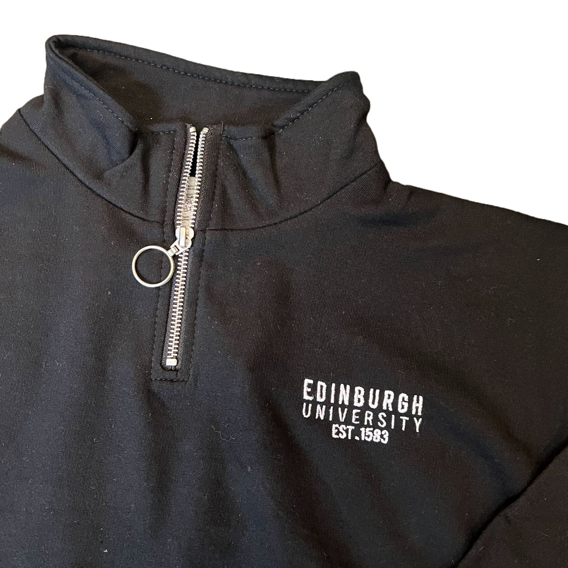Close up of the Black quarter zip cropped sweatshirt with 'Edinburgh University Est. 1583' embroidered in white.