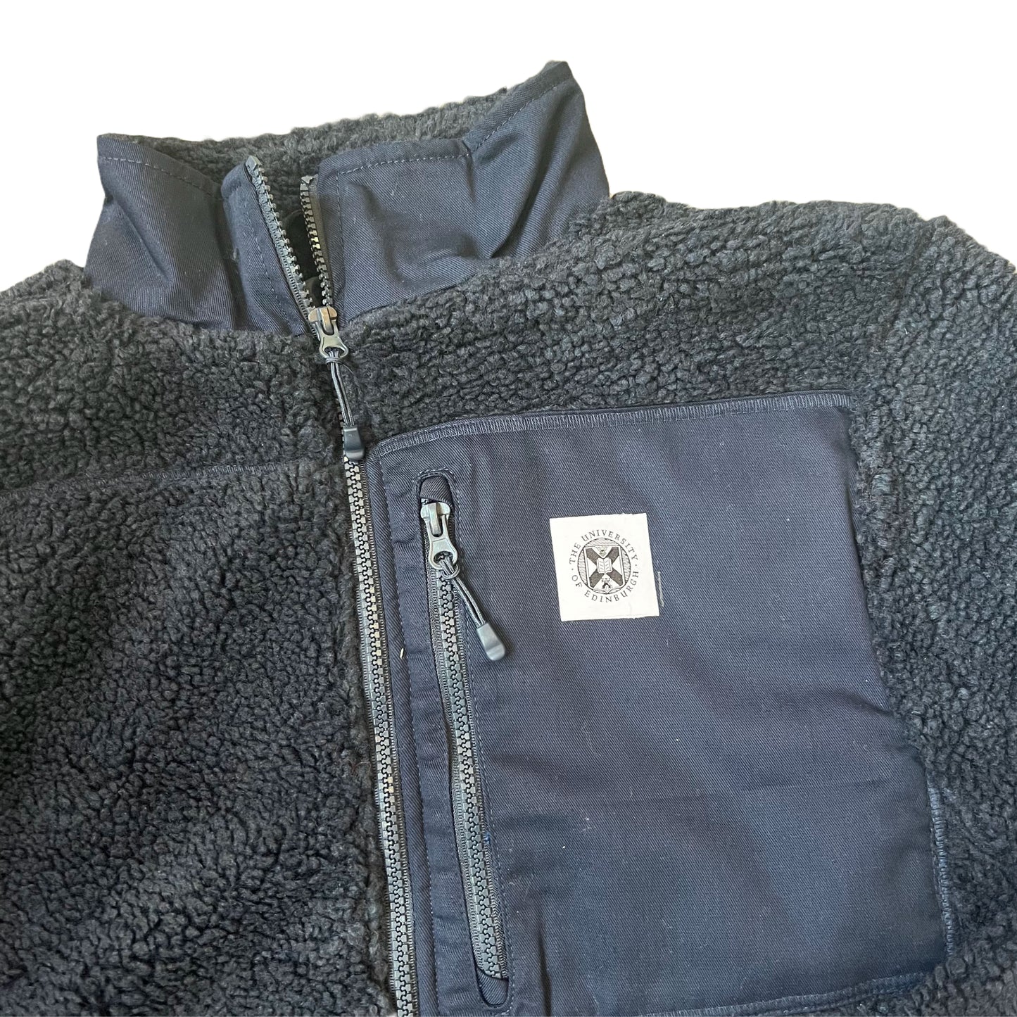 Closeup of pocket with stitched university crest label on navy fleece sherpa jacket.