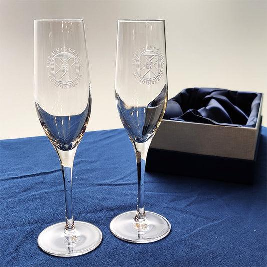 Crystal champagne flutes featuring crest engraving next to a presentation box.