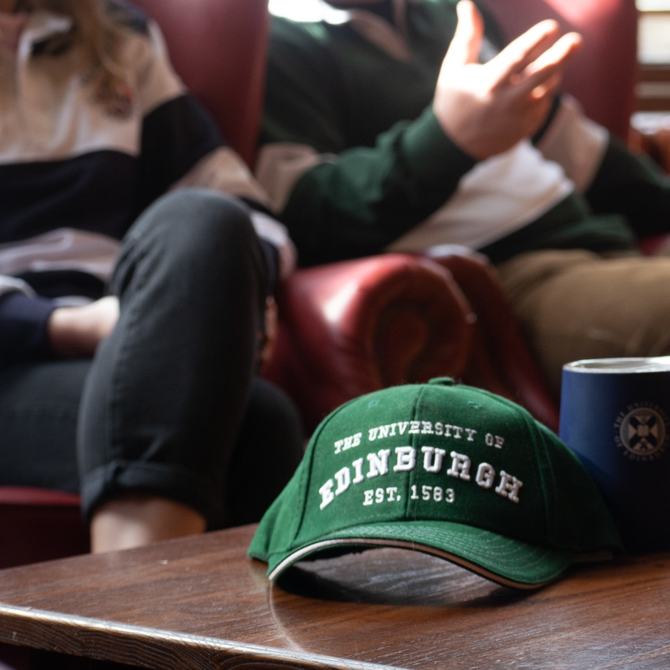 Established design baseball cap in green sitting on a table next to thermal tulip tumbler in navy