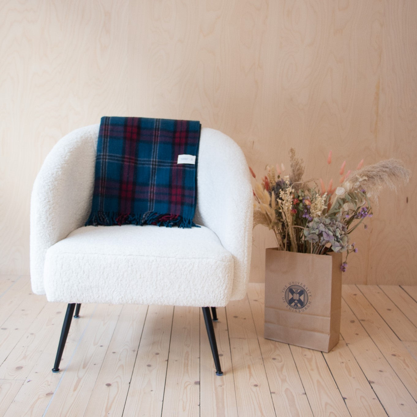 university tartan blanket on white chair, next to paper bag with flower