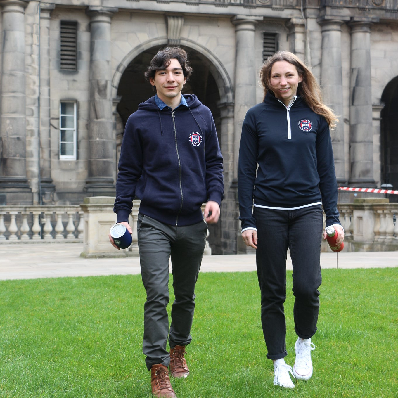 2 models walking in the old college quad, one wearing the sports midlayer in navy, one wearing the premium zipped embroidered hoodie in navy 