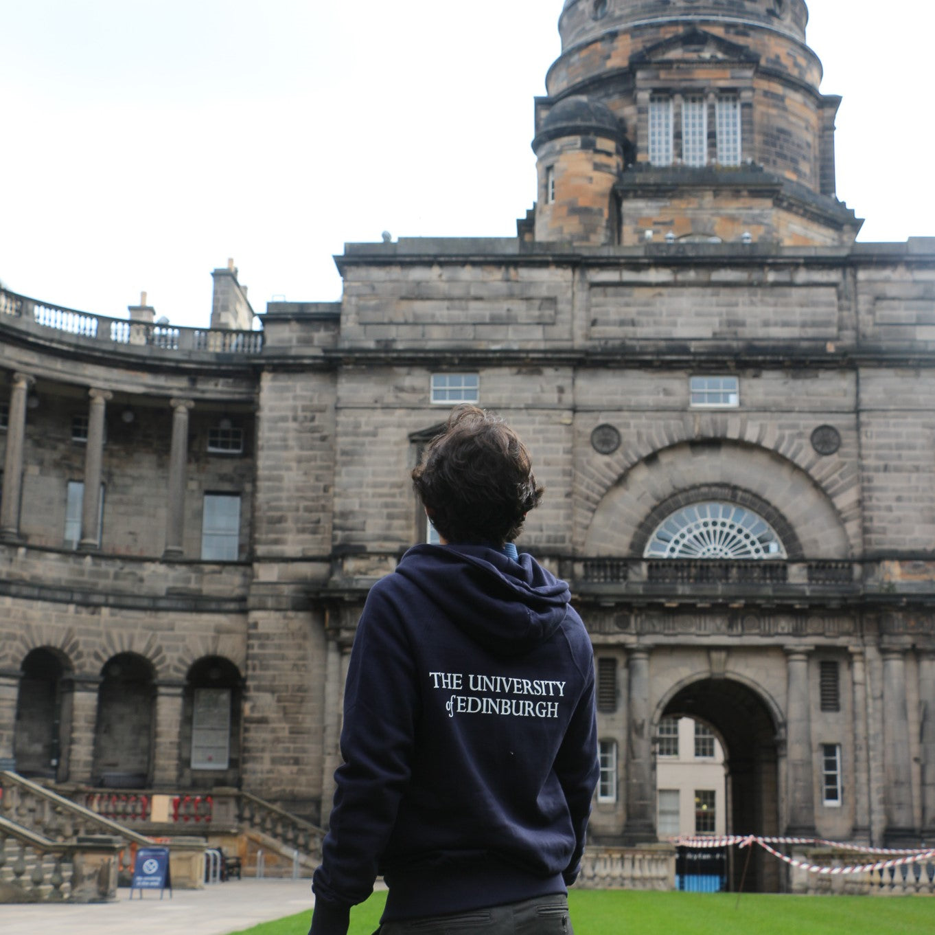 our model wears the premium embroidered zipped hoodie in navy, pictured from behind. The back features 'the university of edinburgh' in white print