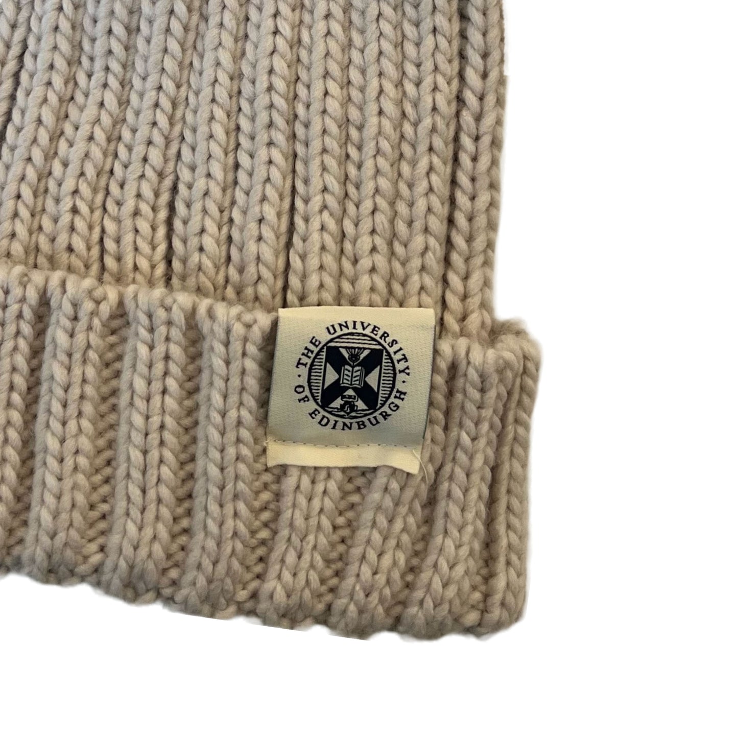 close up of oatmeal beanie with brown pom pom and woven tag featuring university crest in navy