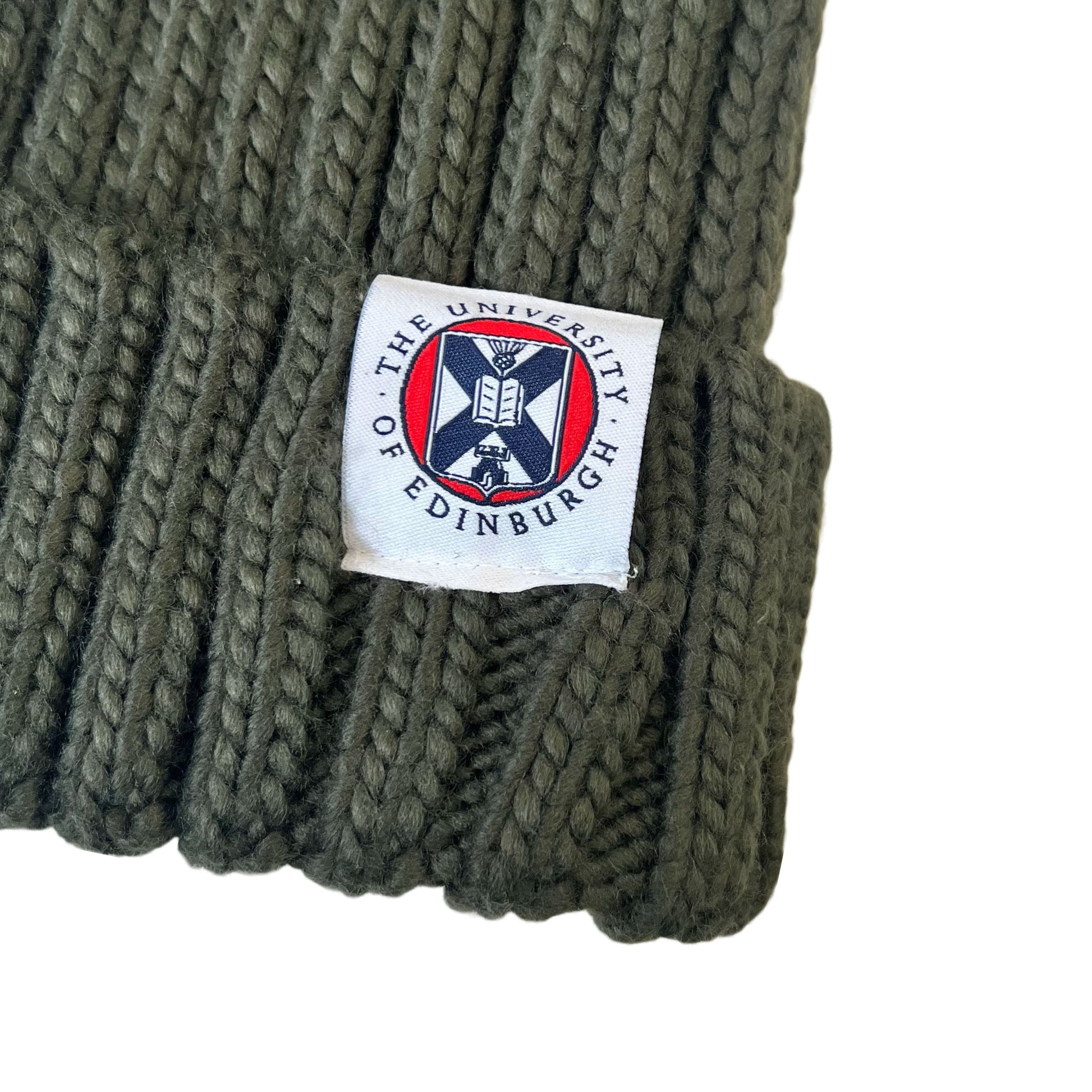close up of Olive Green knit beanie with faux fur pom pom and woven label featuring university crest