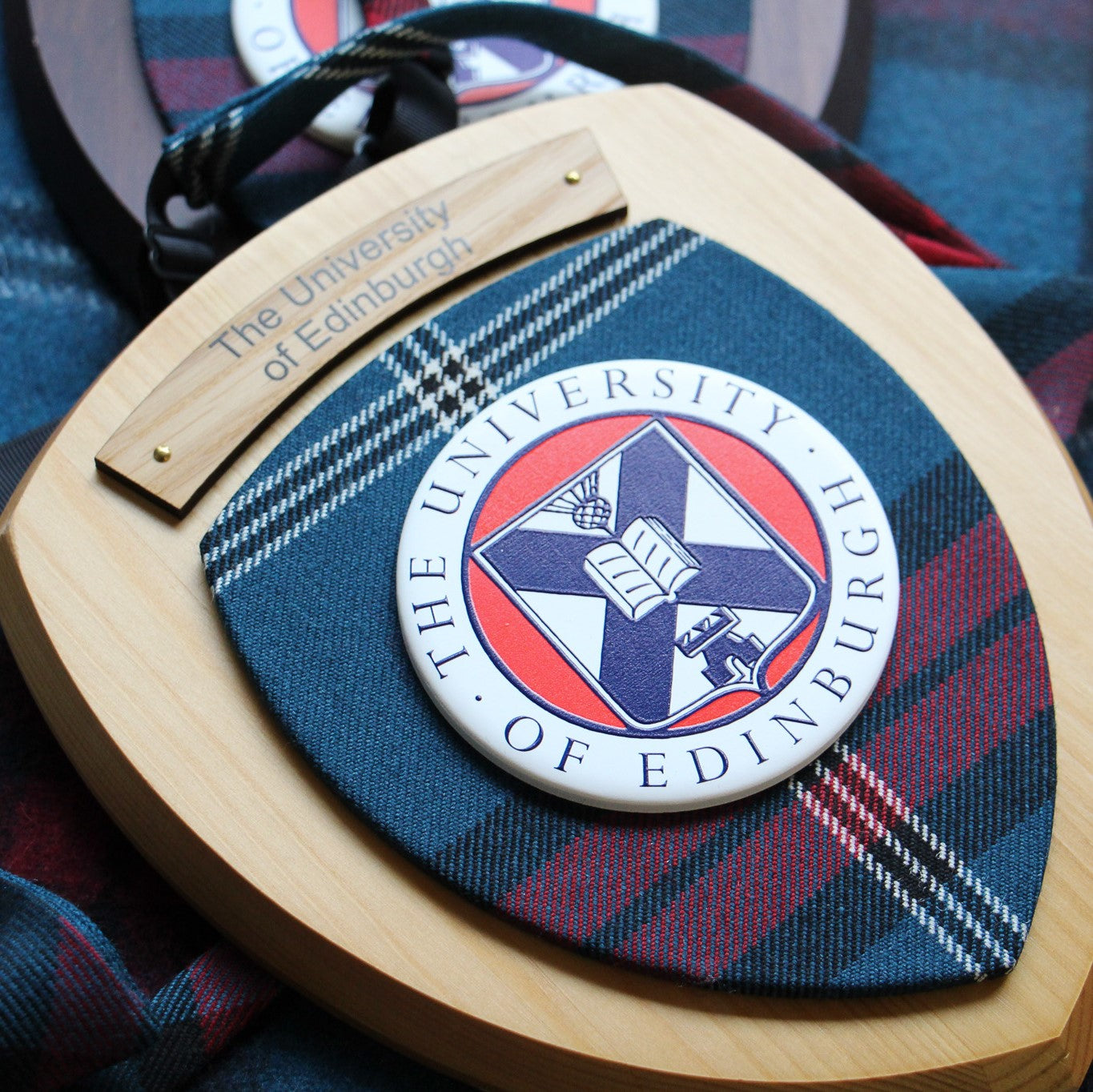 Wall plaque with light wood featuring university tartan, university crest and engrave plate saying 'The University of Edinburgh', pictured next to tartan tie