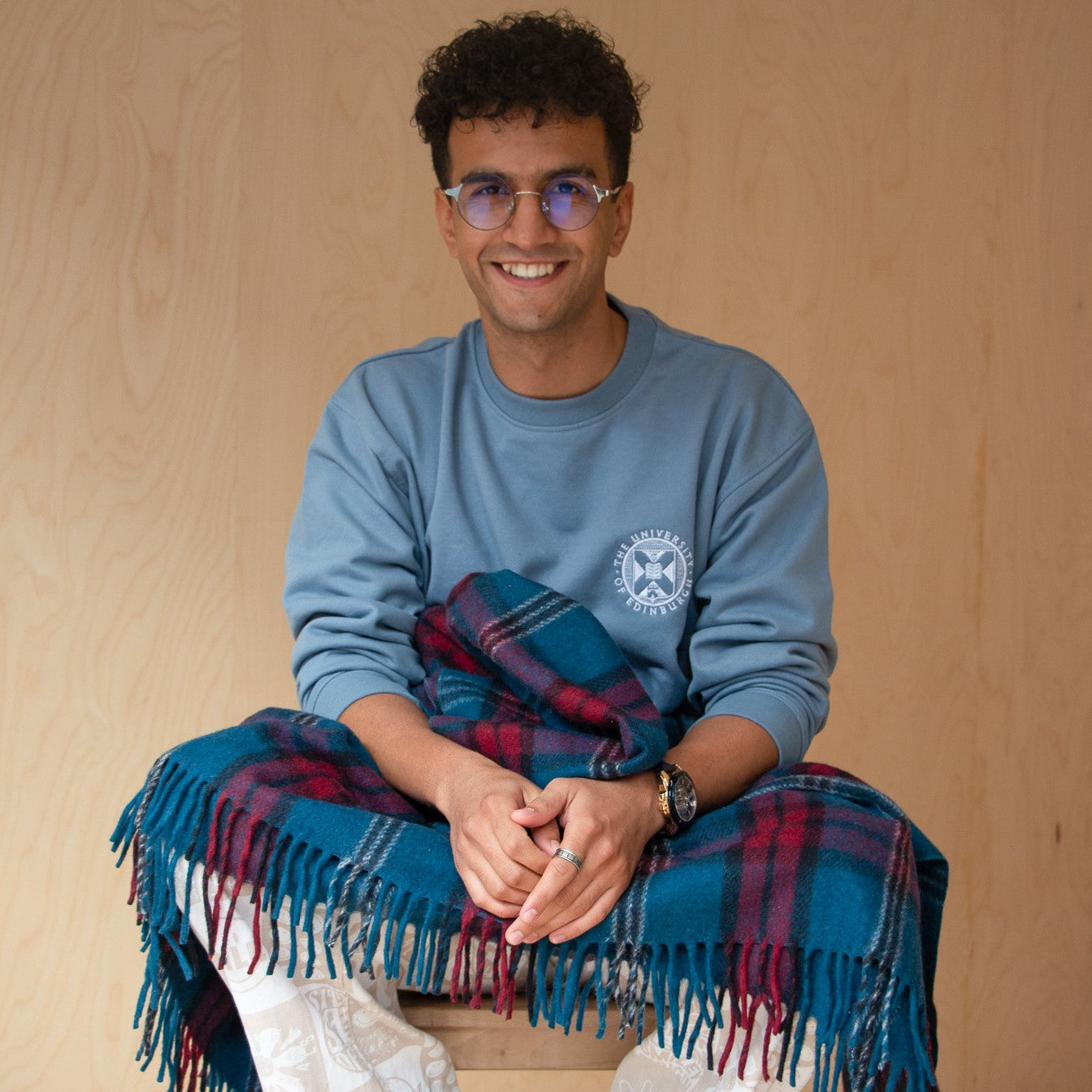 our model wears the stone blue embroidered sweatshirt, holding our university tartan blanket 