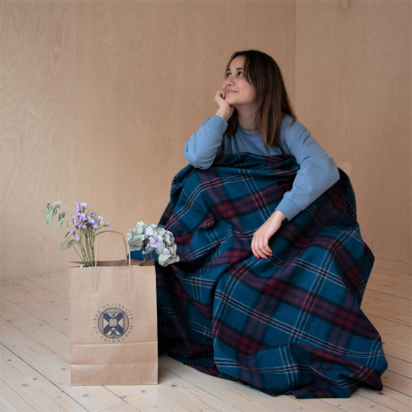 our model under the university tartan blanket wearing the embroidered crest sweatshirt in stone blue