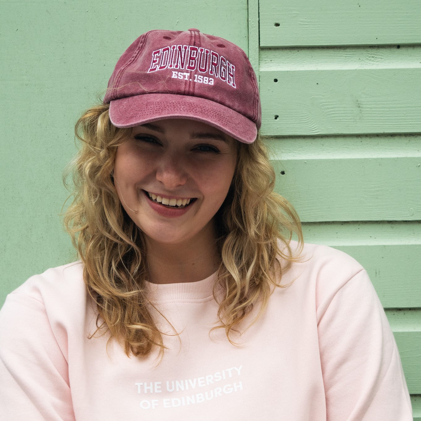 Our model wearing a red baseball cap with red and white text reading 'EDINBURGH EST. 1583'