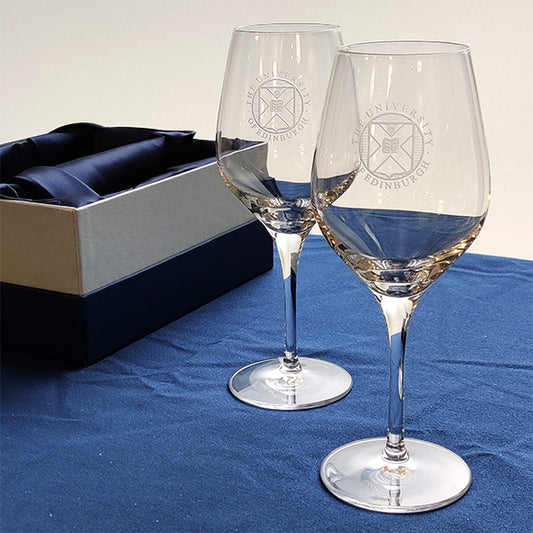 A pair of crystal wine glasses with University crest etching displayed in front of a presentation box. 